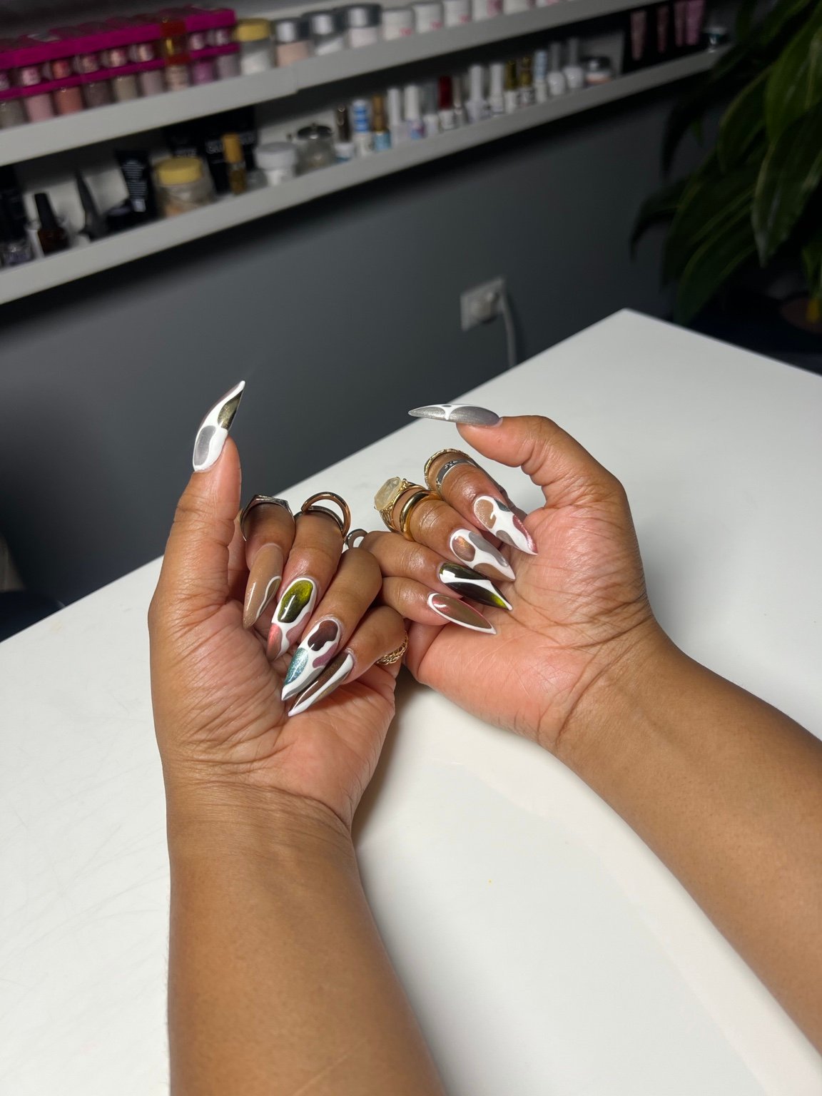 Long chrome stiletto nails with a green accent, resting on the table at Vivid Nails